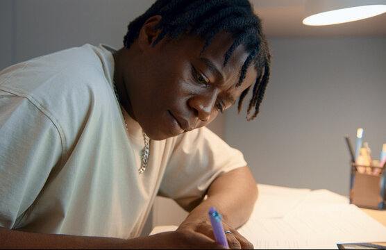 Focused black student studying and taking notes at home desk
