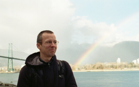 Man with facial expression standing next to a  rainbow.