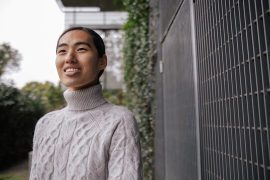 Smiling Individual Outdoors in Knit Sweater by Metal Fence
