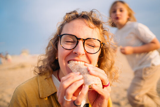 Person biting into wrap at sandy beach