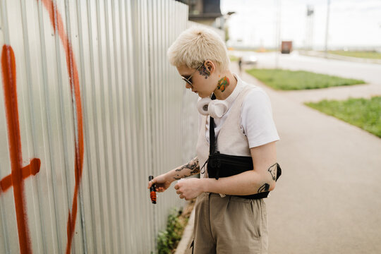 Street Artist Creating Graffiti on Metal Fence with red Paint