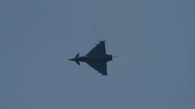 MADRID, SPAIN - OCTOBER 12, 2025: Video of a modern military fighter jet performing a high-speed aerobatic maneuver. The Eurofighter Typhoon banks and turns against a clear blue sky. Footage of air