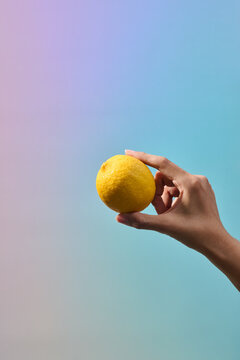 A person's hand gently holds a bright yellow lemon on color background