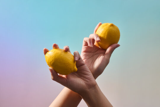 Hands elegantly holding fresh, ripe lemons ON a vibrant background