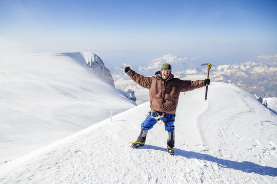 A climber celebrates his ascent to a snow-capped mountain peak 