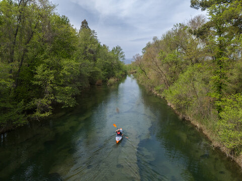 Kayaker paddling a narrow river with clear water and greenery around