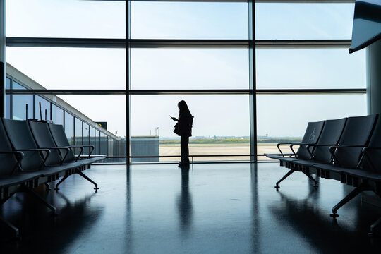 Silhouette of woman using phone at airport window