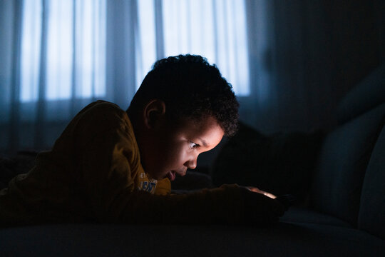 Young boy using smartphone at night with screen light illuminating his