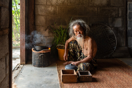 Elderly rural Thai man sits quietly in shadowy home interior