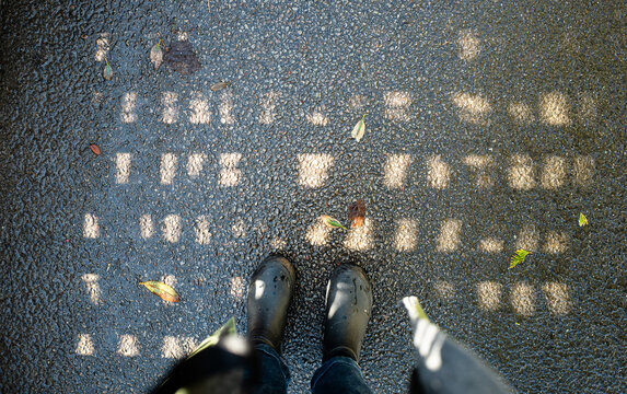 Rain boots standing on a pavement where sunlight is making a pattern