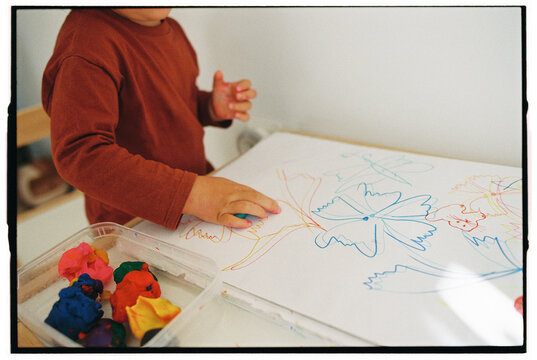 Toddler coloring on paper with plasticine near by