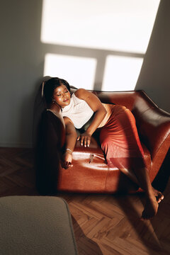 Carefree woman relaxing barefoot on leather chair in sunlight