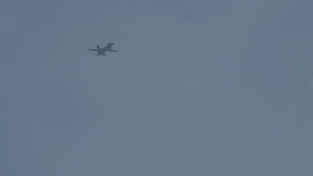 MADRID, SPAIN - OCTOBER 12, 2025: An F-16 Fighting Falcon performs high-speed acrobatic maneuvers, including rolls and turns, against a hazy, overcast sky. The military aircraft showcases its agility