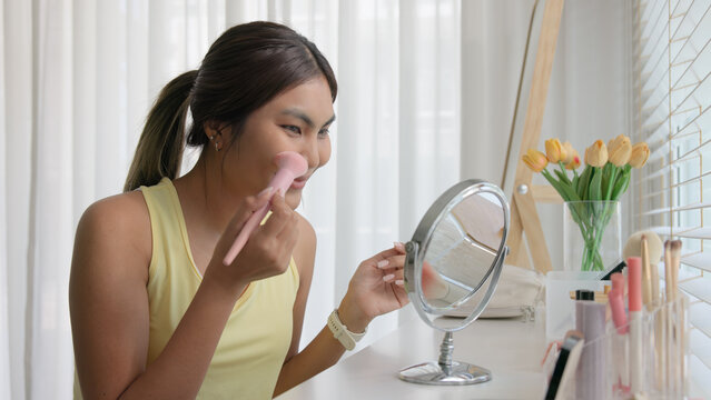 Young adult woman gen z black asia people relax get ready prepare clean makeup apply cream skin care make up getting dressed at home. Look at mirror camera self love anti aging health happy vanity.