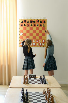 Girls Learning Chess Moves on a Wall Board
