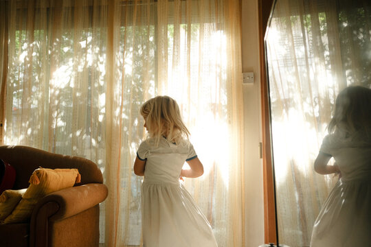 Young girl in a white dress twirls in soft light near sheer curtains