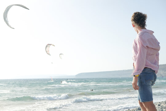 Kitesurfing enthusiast watches as multiple kites glide 