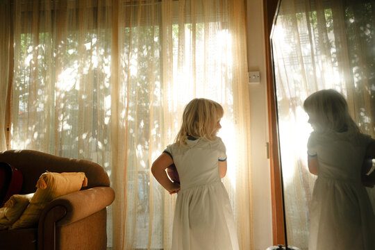 Child standing near window in sunlight, reflection visible in mirror