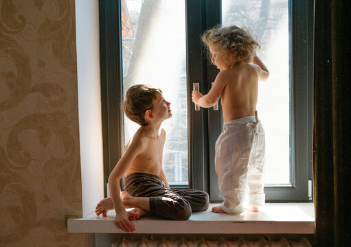 
two brothers are sitting on the windowsill by the window