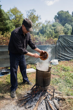 Chef preparing food in a large pot over a wood fire