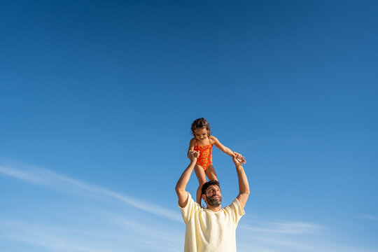 Father and toddler sharing a cute moment under a clear blue sky.