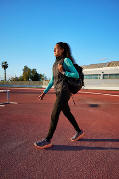 Young athlete walking on track at sunset with backpack