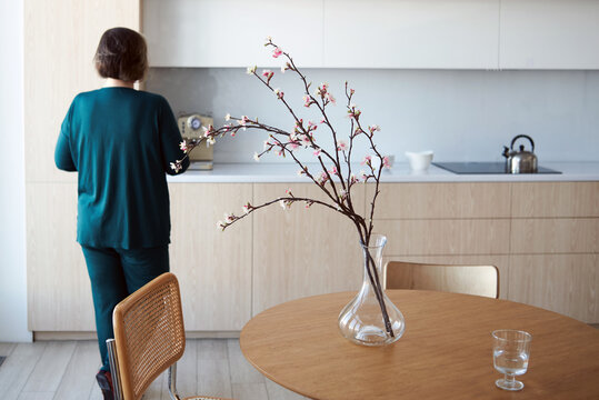 Woman preparing food in kitchen with floral arrangement on table
