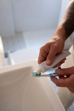 Person Squeezing Toothpaste Onto a Toothbrush in Bathroom