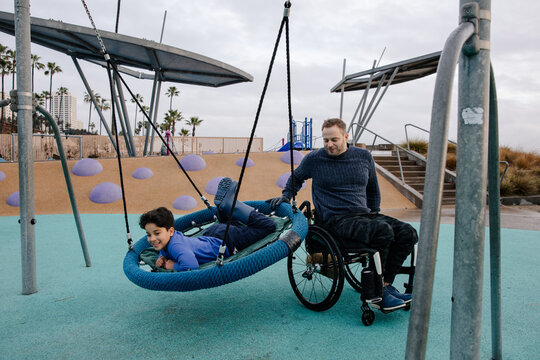 Father Supporting Son on Swing at Inclusive Playground