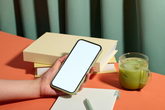 A modern workspace featuring a smartphone, matcha latte and books.
