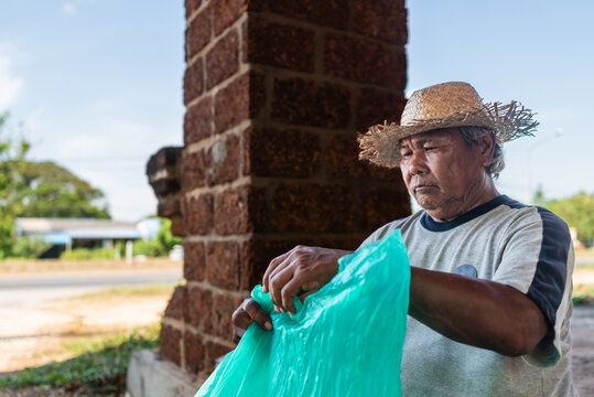 Elderly Thai Man Sitting on Roadside, Tying a Bag of Plastic Bottles