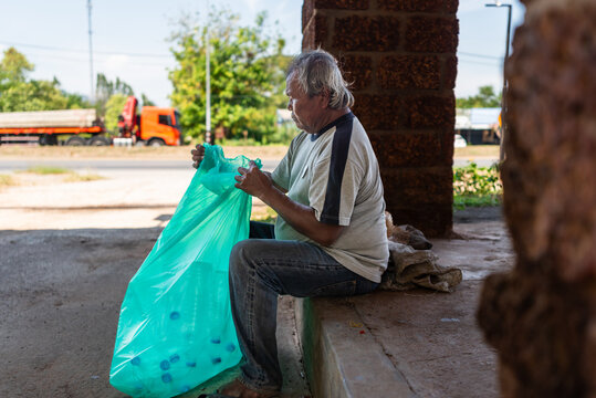 Elderly Thai Man Sitting on Roadside, Tying a Bag of Plastic Bottles