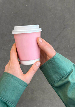 Female hands in green shirt holding blank pink coffee cup.