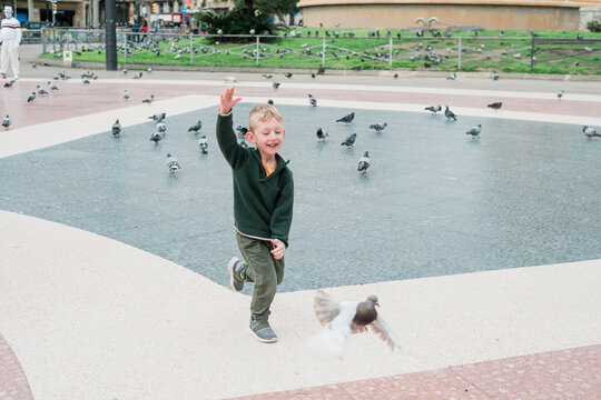 A young boy laughs while he runs with the pigeons in a city park