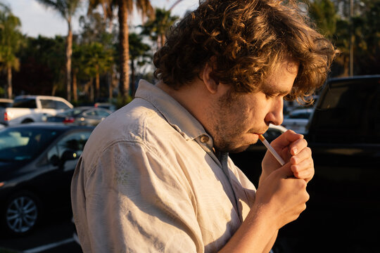 Man lighting a cigarette in a parking lot