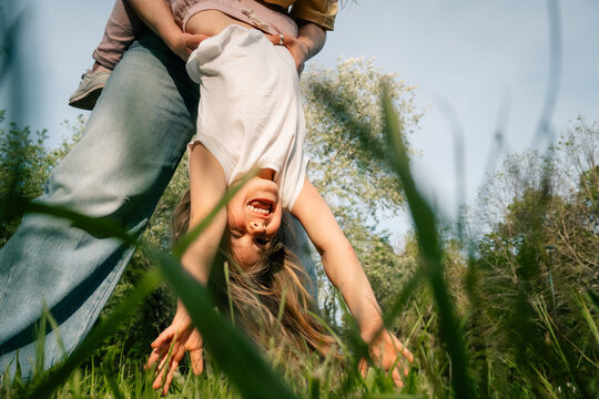  Laughing child upside down in grass held by legs outdoors