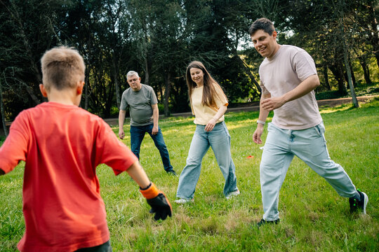Group of four people playing soccer on green grass under trees