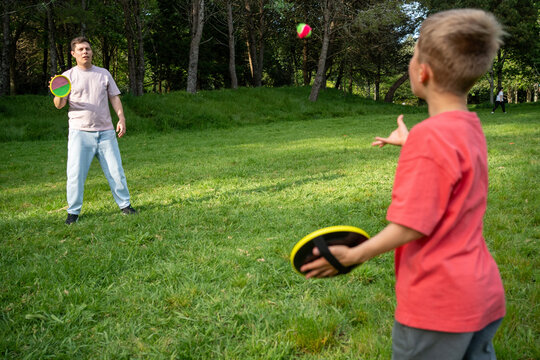 Man and Boy Play Catch With Discs in Park on Sunny Day