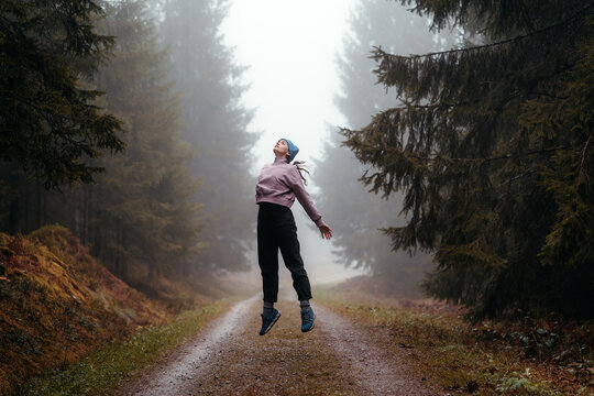 Woman jumping and levitating in a winter forest with fog
