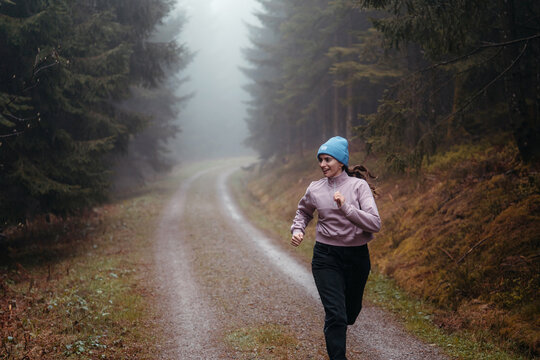 Smiling woman running and exercising in the forest