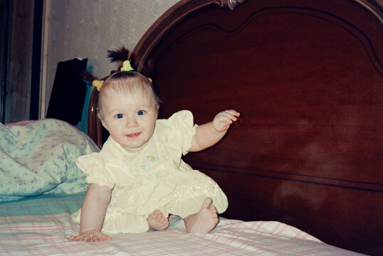 Smiling Baby Sitting on Bed with Wooden Headboard