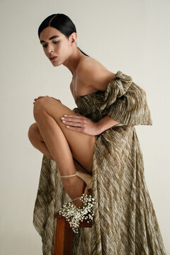 Elegant strapless dress with slit crouching on wooden stool 