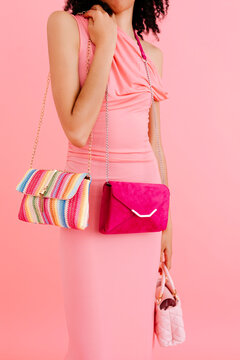 Anonymous woman showing colorful handbags on pink background