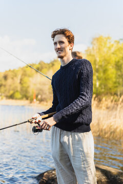 Smiling Young Man with Fishing Rod Enjoying the Day by the Lake