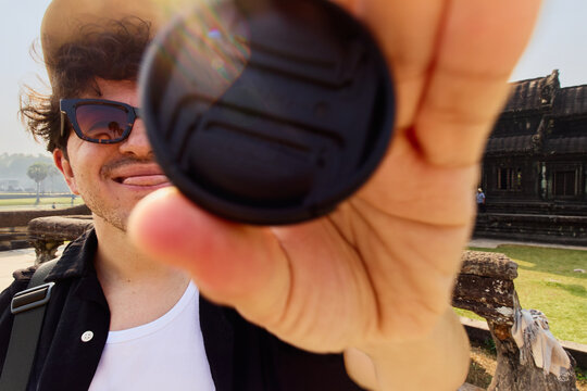 Playful moment of man Holding a Camera Lens Cap Toward the Frame