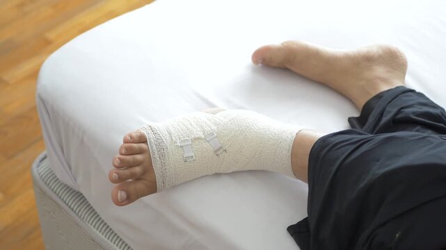Close up shot of person with leg wrapped in a bandage, lying on bed at home, recovering from injury