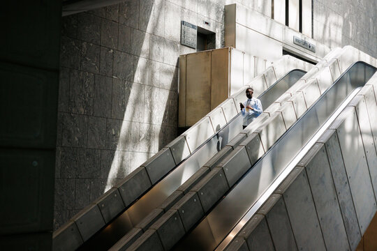 Man Ascending with Drink and Phone in Modern Space