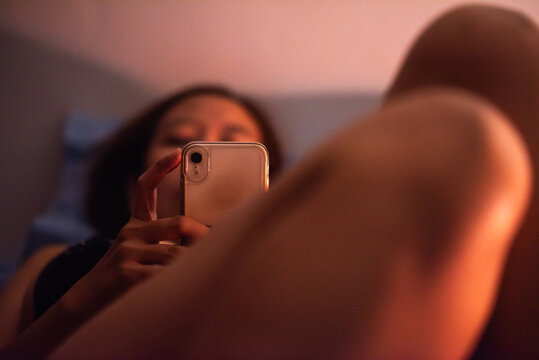 Tired working woman relaxing in bed with phone at night