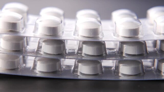 Close up of white round pills in blister packs stacked on a dark surface
