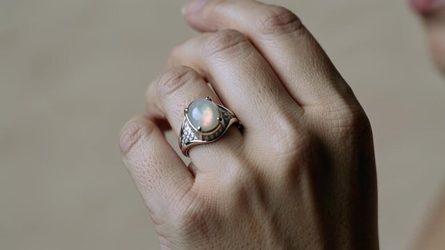 Closeup of woman hand wearing silver ring with opal gemstone, luxury jewelry detail, horizontal video, elegant accessory, classic style.